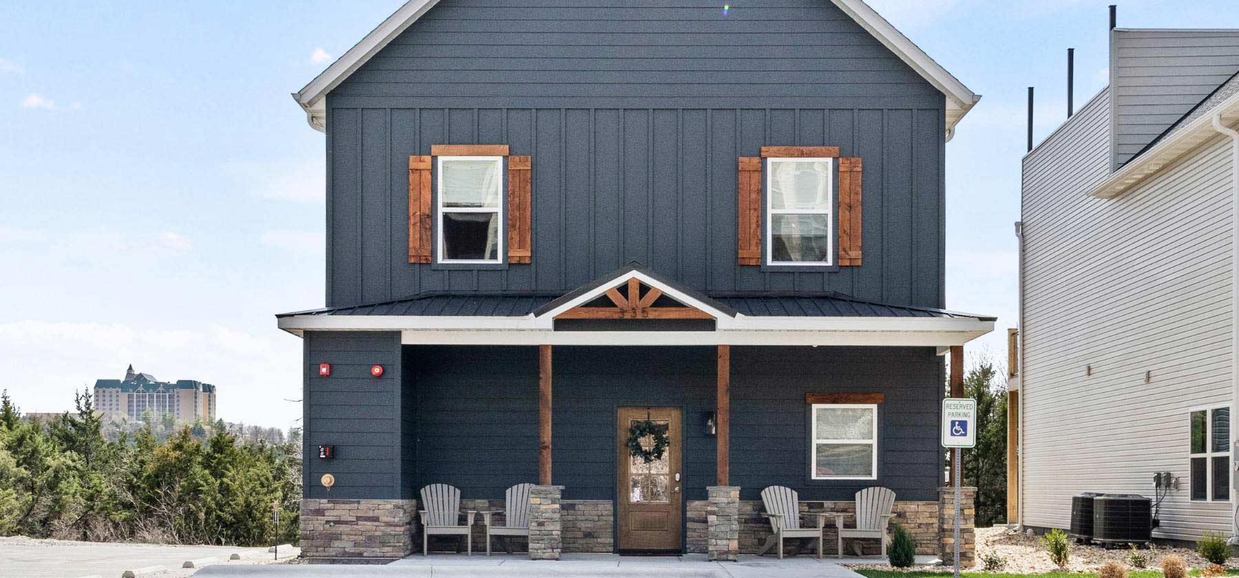 Modern two-story house with dark siding, wooden shutters, and a covered porch.