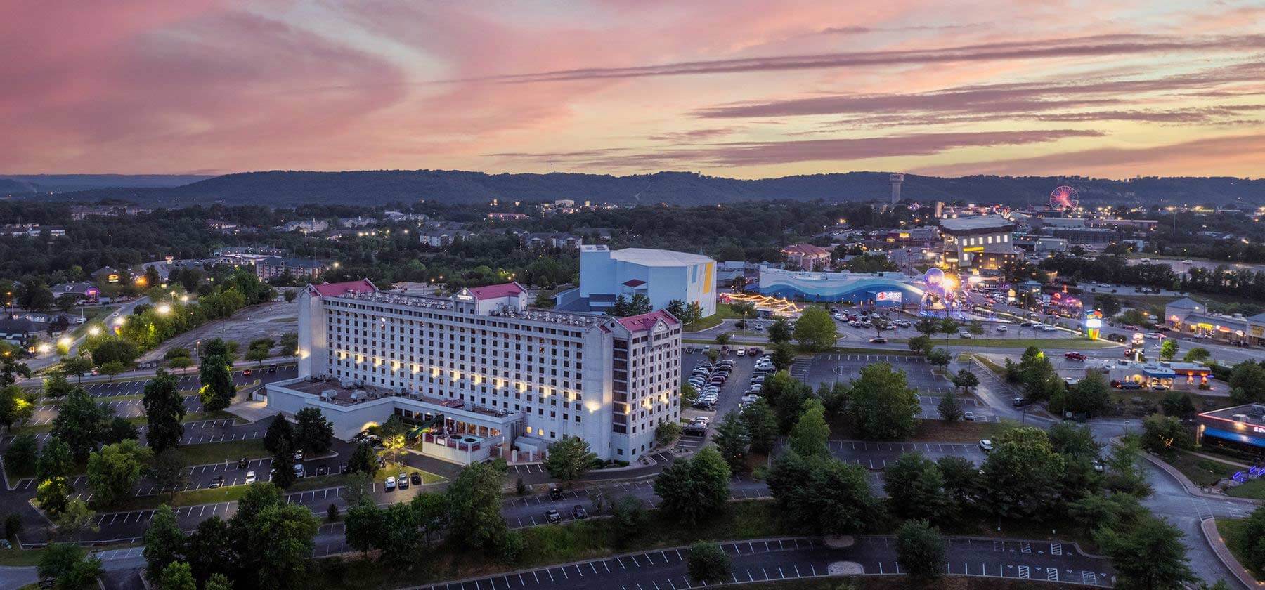 Aerial view of a lit-up cityscape during twilight with a large hotel in the foreground.