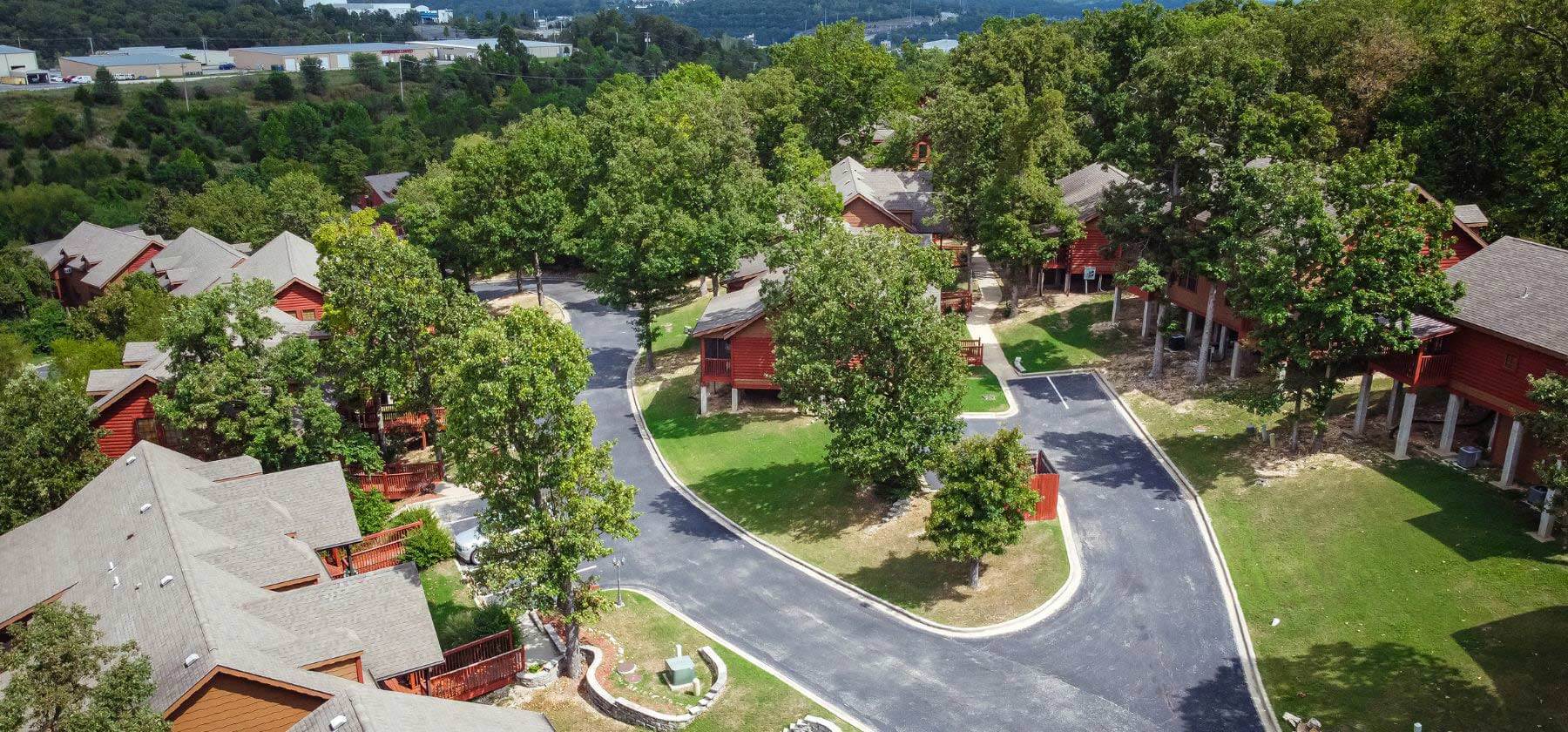 Aerial view of a winding road amidst red-roofed houses surrounded by green trees.