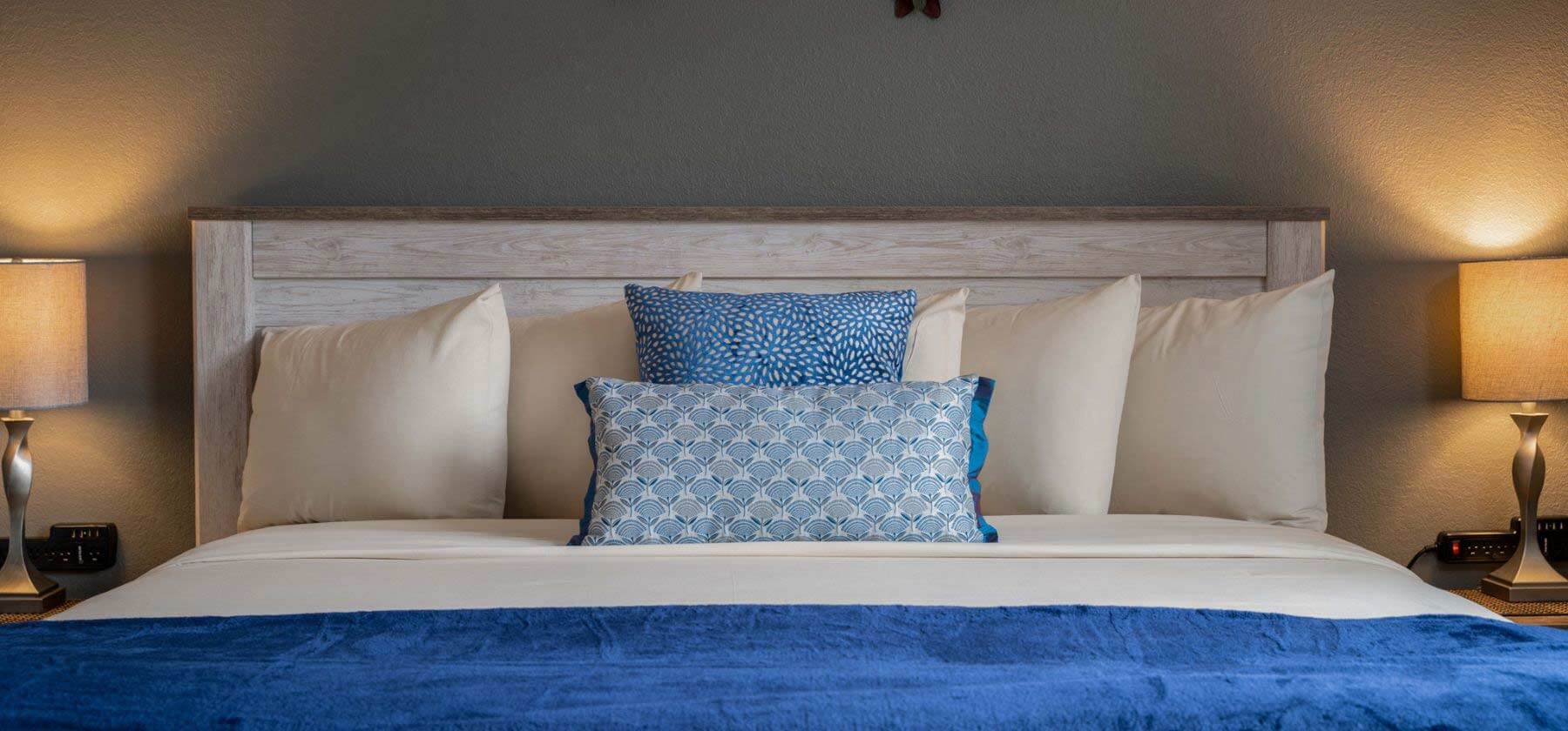 Elegant bed with white and blue pillows, blue throw blanket, and bedside lamps.