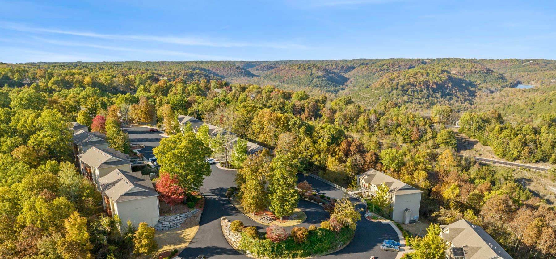 Aerial view of a resort with cabins amid colorful autumn trees and rolling hills.